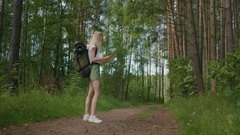 Slow-motion-of-a-young-tourist-woman-with-a-road-card-and-a-compass-in-the-woods-searching-for-the-footpath.